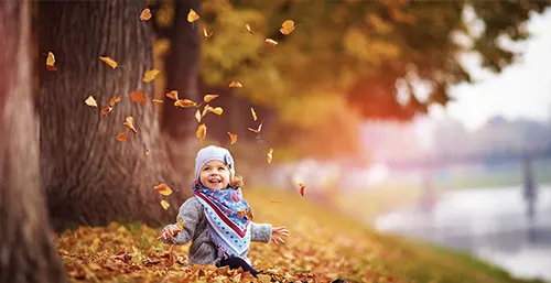 Odporność u dzieci - jak ją poprawić? Jak wzmocnić odporność u dzieci? Mała uśmiechnięta dziewczynka siedzi w jesiennych liściach.