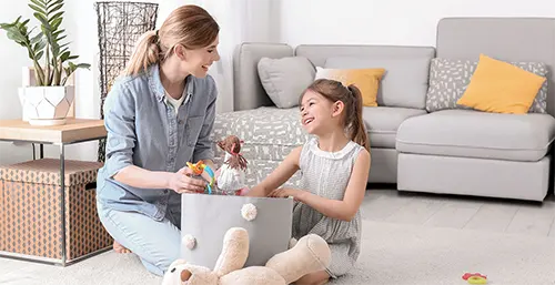 Jak nauczyć dziecko sprzątać? Nauka sprzątania. Mama uczy córeczkę, jak sprzątać po sobie zabawki.